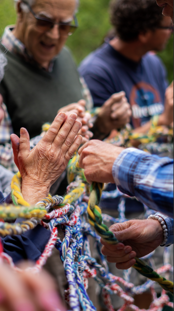 A detail of the moving threads artistic workshop by Paola Anziché. The hands of the participants are working together on weaving coloured ropes.