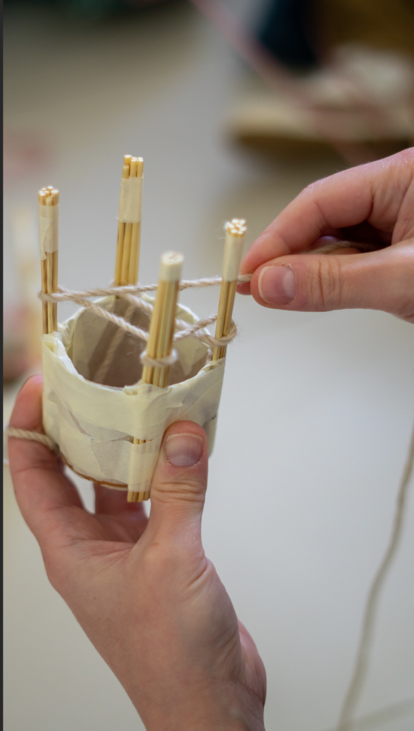 A detail from the Moving Thread workshop by Paola Anziché: a person's hands are working in weaving a thin rope in between the wooden part of a small handheld loom.